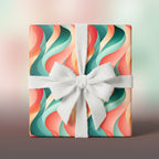 Gift box in modern abstract wrapping paper with teal, peach, and cream waves, tied with a textured white ribbon.