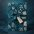 Elegant gift wrapped in dark blue floral wrapping paper with teal ribbon and "Oceanic Blooms" tag.