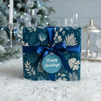 Elegant teal floral wrapping paper with a dark blue satin bow and "Happy Holidays" tag.