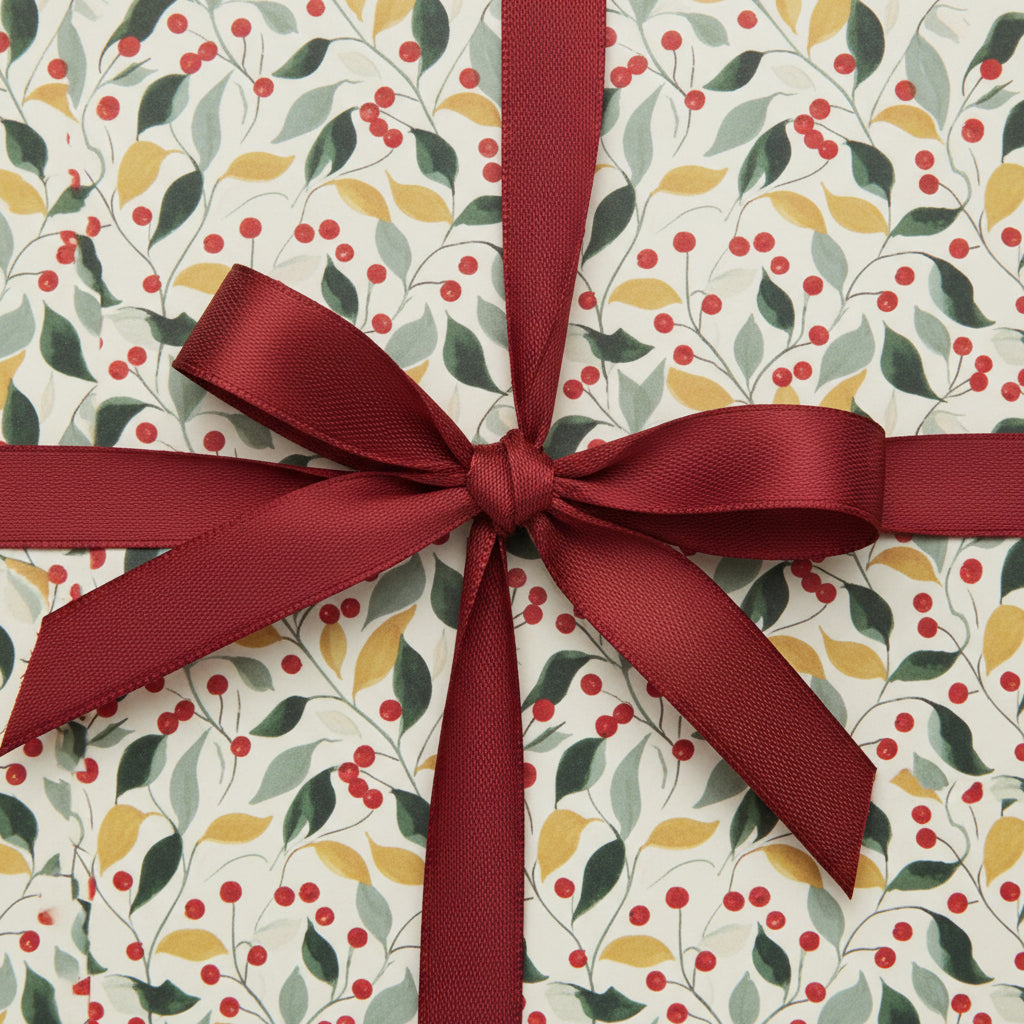 Holiday gift wrapped in botanical Christmas wrapping paper with red berry and leaf pattern, tied with a satin burgundy bow.