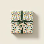 Festive gift wrapped in floral holiday wrapping paper with dark green ribbon and leaf tag.