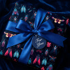 Elegant gift wrapped in dark beetle and butterfly wrapping paper with blue satin ribbon, “For You” tag.