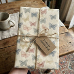 Butterfly patterned wrapping paper on a gift tied with twine and a tag on a wood table.