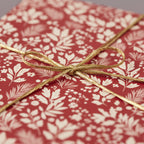 Close-up of a gift wrapped in red floral wrapping paper with a gold ribbon, perfect for Christmas or birthdays.