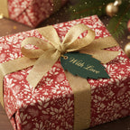 Elegant red floral wrapping paper with gold ribbon and "With Love" leaf tag, perfect Christmas gift wrap.