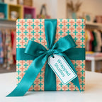 Modern geometric wrapping paper in teal and peach with a large satin bow by Wrapped Studios.