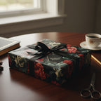 Elegant gift wrapped in dark floral wrapping paper with a black satin ribbon and gift tag, resting on a wood table.