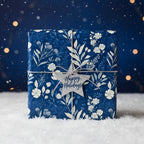 Elegant navy Christmas gift wrap with white floral pattern and silver "Happy Holidays" star tag.