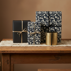 Elegant gifts wrapped in floral wrapping paper and black gift wrap with gold and twine ribbons on a wooden table.