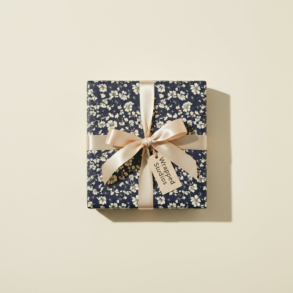 Square gift box wrapped in navy floral wrapping paper with a champagne satin ribbon and bow.