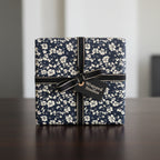 Elegant gift box wrapped in navy floral wrapping paper with black ribbon and "Wrapped Studios" tag.