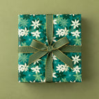 Square gift wrapped in teal floral wrapping paper with green ribbon and gold trim.