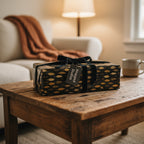 Rectangular gift wrapped in elegant leaf print paper with a black velvet ribbon on a rustic wood table.