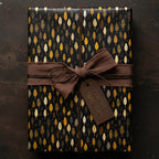 Elegant gift wrapped in black and gold leaf pattern paper with brown ribbon and "Crafted with Care" tag.