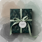 Square gift box in dark green floral wrapping paper with sage ribbon and bow.