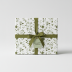 Elegant gift box wrapped in white floral wrapping paper with a sage green ribbon and tag.