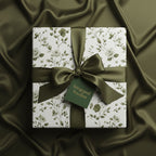 Elegant gift box with olive floral wrapping paper and matching satin ribbon on draped fabric.