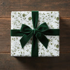 Elegant floral wrapping paper with a green velvet ribbon on a square gift box, set on wood.