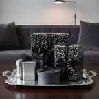 Elegant gifts wrapped in black and silver floral wrapping paper, tied with satin ribbons on a serving tray.