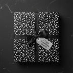 Black and silver floral wrapping paper with satin ribbon and gift tag, perfect for elegant gift-giving.