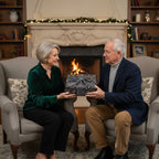 Couple exchanging gift wrapped in elegant floral wrapping paper with gray ribbon, in front of fireplace.