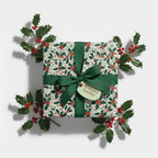 Square gift wrapped in floral Christmas wrapping paper with red holly berries and a green ribbon.