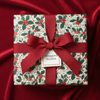 Elegant Christmas gift wrapped in festive holly berry floral wrapping paper with a red ribbon.