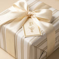 Luxury cream and gold striped wrapping paper with a satin ribbon bow and gift tag by Wrapped Studios.