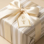 Luxury cream and gold striped wrapping paper with a satin ribbon bow and gift tag by Wrapped Studios.