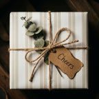 Rustic striped wrapping paper with twine, eucalyptus, and a Cheers tag by Wrapped Studios.