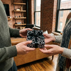 Hands exchanging a gift in modern black and white polka dot wrapping paper with a satin bow. Wrapped Studios.