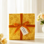 Elegant gold floral wrapping paper on a square gift box with a velvet amber ribbon and bow.
