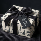 Luxury travel gift wrap with black world landmarks and a velvet bow by Wrapped Studios.