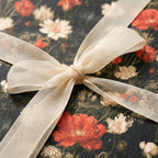 Moody dark floral wrapping paper with red poppies and a cream ribbon bow, by Wrapped Studios.