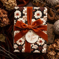 Vintage floral wrapping paper with white daisies, a rust velvet bow, and a "With Love" tag by Wrapped Studios.