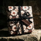 Vintage floral gift wrap with white daisies and black yarn bow on a rustic gift box. Wrapped Studios.