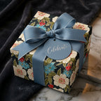 Luxury floral wrapping paper with a dusty blue ribbon and 'Celebrate' tag by Wrapped Studios.