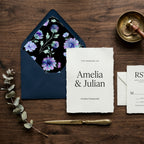 Elegant purple floral envelope liner and wedding invitation set on a wood table by Wrapped Studios.