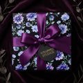 Elegant purple floral wrapping paper with a satin bow on a gift box by Wrapped Studios.