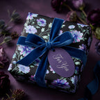 Elegant dark floral wrapping paper with a blue velvet bow on a luxury gift box by Wrapped Studios.