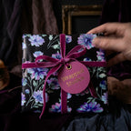 Luxury dark floral wrapping paper with purple flowers and magenta velvet bow by Wrapped Studios.
