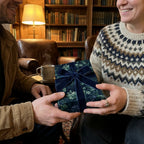 Couple exchanging holiday gift in dark green floral wrapping paper with velvet bow by Wrapped Studios.