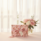Elegant floral wrapping paper in pink with a satin ribbon and "For You With Love" tag, next to a matching rose bouquet.
