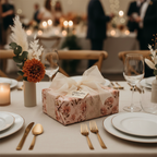 Elegant floral wedding gift wrapped in blush pink paper with a sheer cream bow, on a beautifully set table with warm candlelight.