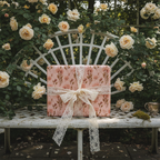 Pink floral luxury gift wrap with delicate lace ribbon on a white garden bench, surrounded by blooming roses, perfect for weddings or birthdays.