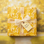 Square gift wrapped in yellow floral wrapping paper with sheer ribbon and "Warm Regards" tag.