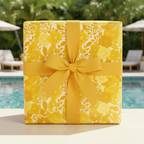 Square gift wrapped in yellow floral wrapping paper with matching grosgrain ribbon, poolside.