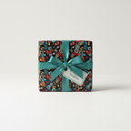 Square gift box wrapped in colorful circle patterned wrapping paper with a teal ribbon.