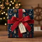 Nautical Christmas wrapping paper with anchors, boats, and houses on a dark blue background, tied with a red ribbon and bow.
