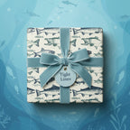 Square gift box in fish-themed wrapping paper with light blue velvet ribbon.